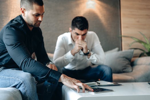 Two men engaged in a serious discussion, analyzing cryptocurrency data on a tablet indoors.