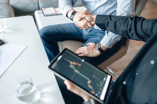 Business professionals shaking hands with a tablet displaying financial graphs.