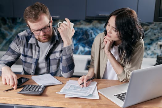 A couple reviews bills and documents on a laptop while discussing household finances.